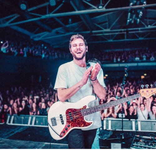 Milky Chance member in a light bue t-shirt and black jeans clapping on the stage.